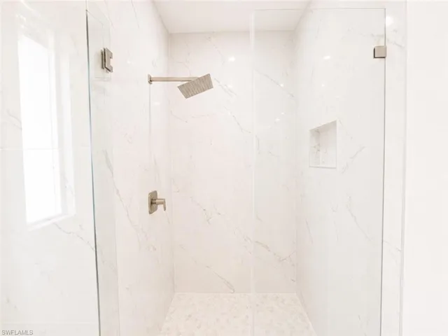 Glass-enclosed shower featuring large format tile walls, a rain shower head, brushed nickel fixtures, a built-in shower niche, and a mosaic tile floor