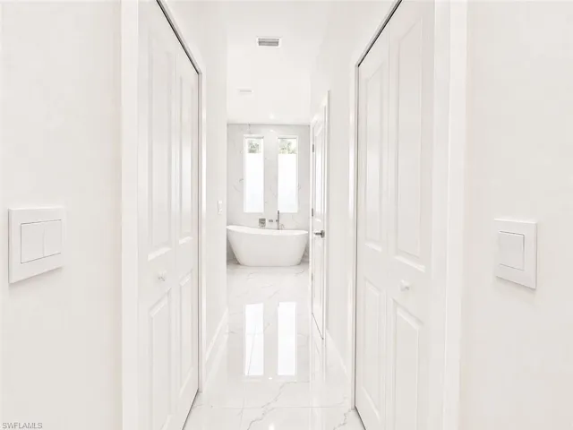 Bright hallway with white walls and bi-fold doors, leading to a bathroom with a freestanding soaking tub