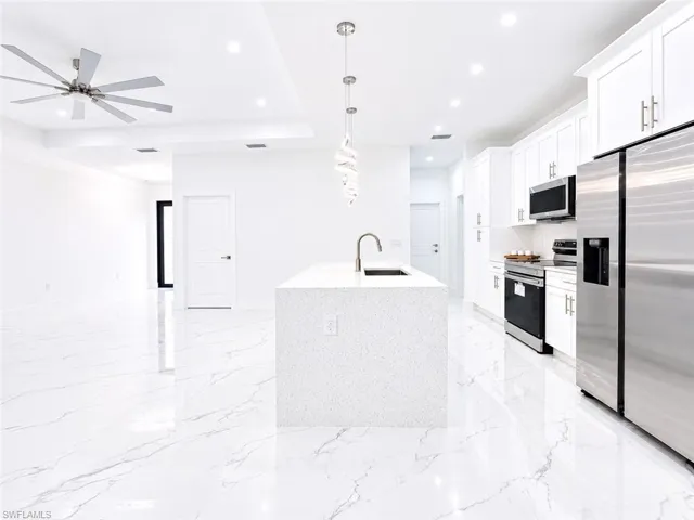 Contemporary kitchen with white cabinetry, stainless steel appliances, and a central island featuring a sink and a modern pendant light fixture