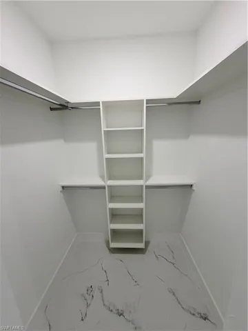 Spacious closet for him featuring light marble finish flooring