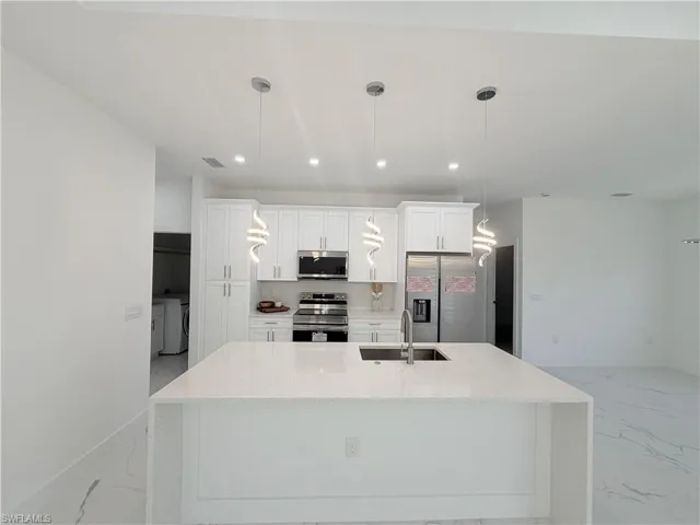 Kitchen featuring light marble finish flooring, appliances with stainless steel finishes, decorative light fixtures, white cabinets, and recessed lighting