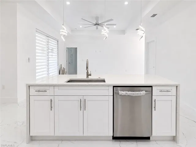 Kitchen island featuring white shaker cabinetry, an undermount sink with a gooseneck faucet, a stainless steel dishwasher, and a light-toned countertop