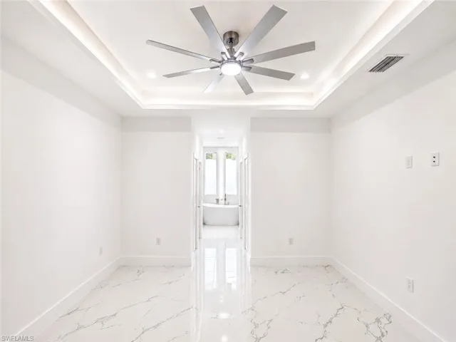 Room featuring a modern ceiling fan with integrated lighting, recessed tray ceiling with cove lighting, and glossy marble-look flooring