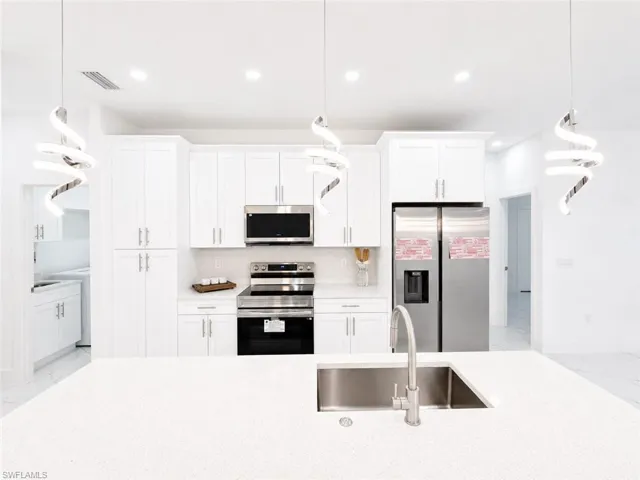 Spacious kitchen featuring white shaker cabinetry, stainless steel appliances, a white quartz island countertop with an undermount sink, and recessed lighting