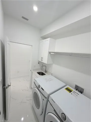 Laundry room with light marble finish flooring, cabinet space, washing machine and dryer, and recessed lighting