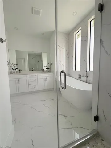 Full bath with a freestanding tub, double vanity, a marble finish shower, and recessed lighting