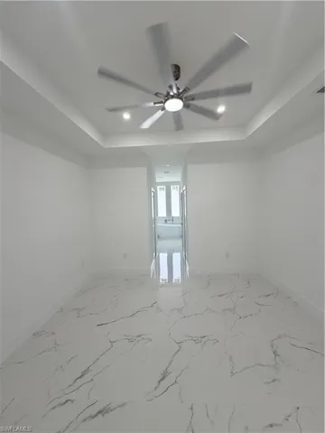 Empty room featuring a raised ceiling, light marble finish floors, recessed lighting, and ceiling fan