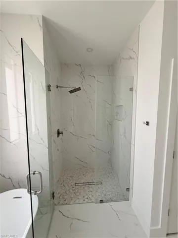 Full bath featuring marble tiled floors, a marble finish shower, and a freestanding tub