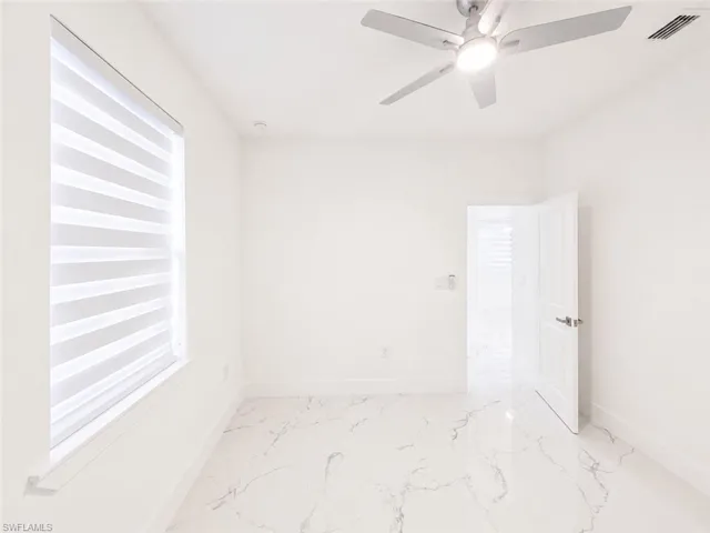 Bright room featuring large format tile flooring, a window with layered shades, a contemporary ceiling fan with integrated lighting, and a modern interior door with brushed nickel hardware
