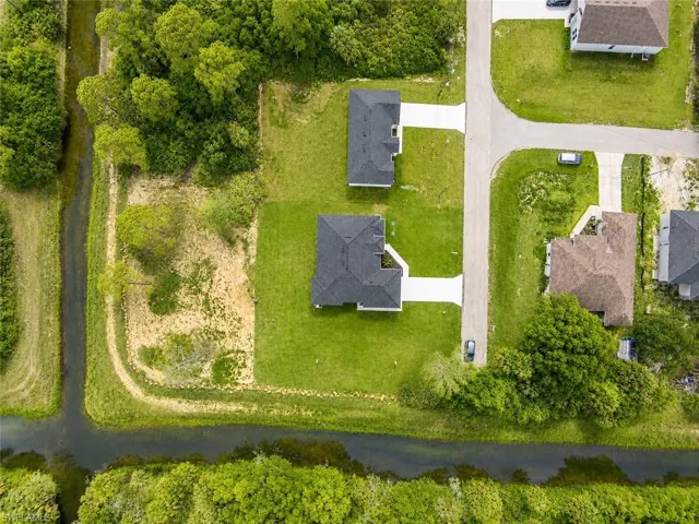 Aerial perspective of a developed residential property featuring a dark-shingled roof and a light-colored driveway