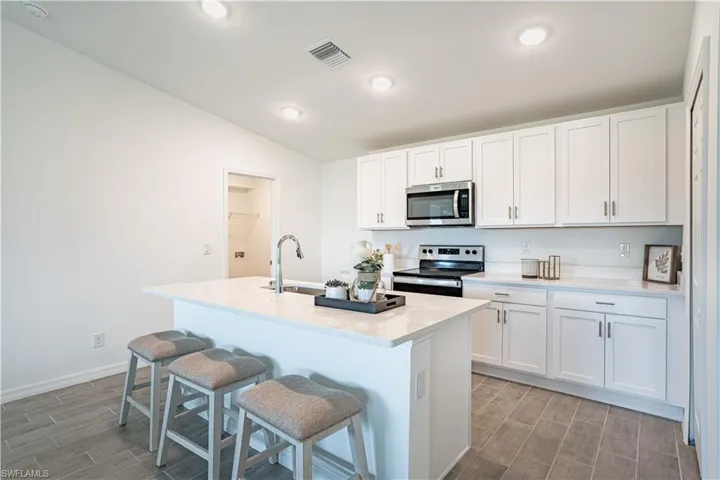 Kitchen featuring stainless steel appliances, white cabinetry, wood tiled floors, a kitchen island with sink, and lofted ceiling