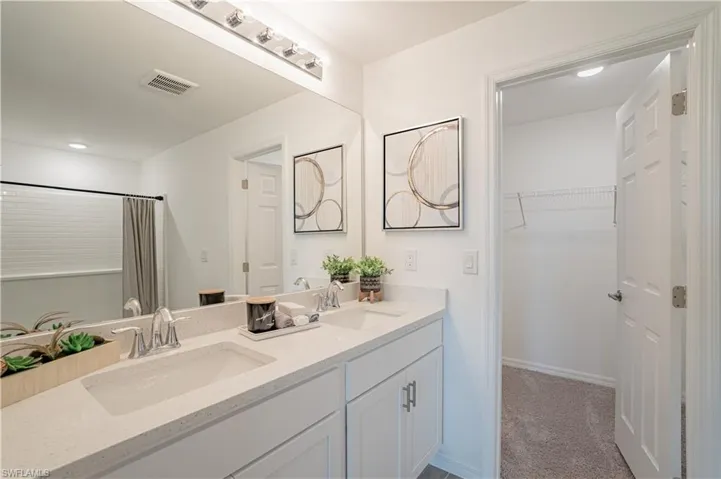Bathroom with double vanity, light colored carpet, curtained shower, and a spacious closet