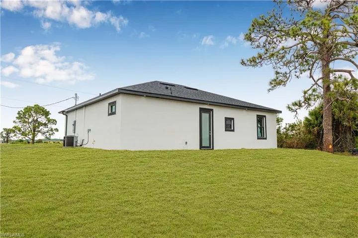 Rear view of property featuring cooling unit, stucco siding, and a yard