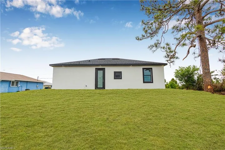 Rear view of property featuring a lawn and stucco siding