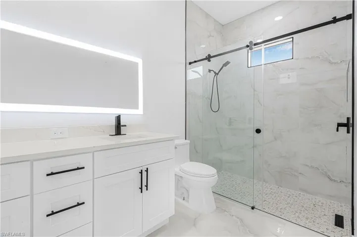 Bathroom featuring a marble finish shower, marble finish floor, toilet, and vanity