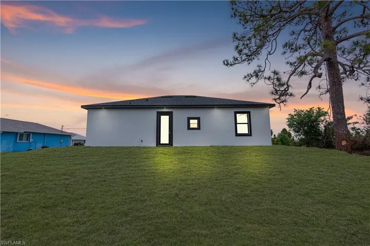 Back of property at dusk with stucco siding and a yard