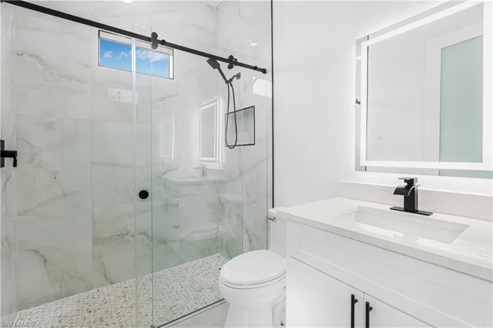 Bathroom featuring toilet, vanity, and a marble finish shower