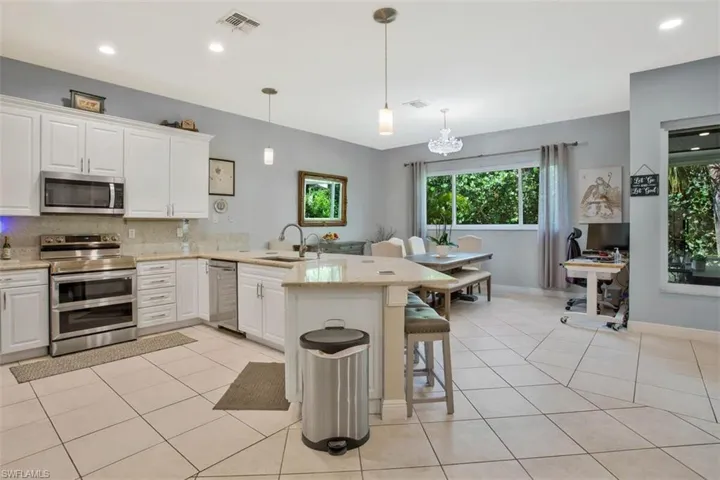 Kitchen with white cabinets, appliances with stainless steel finishes, a kitchen bar, decorative light fixtures, and sink
