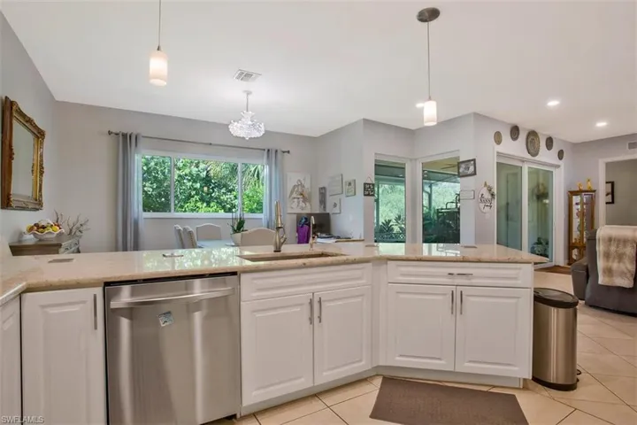 Kitchen featuring stainless steel dishwasher, sink, white cabinetry, and hanging light fixtures