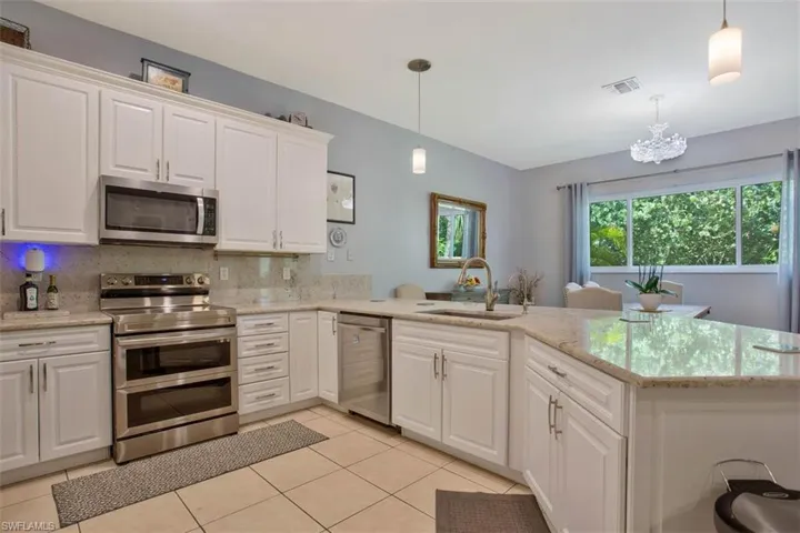 Kitchen featuring kitchen peninsula, sink, pendant lighting, white cabinetry, and appliances with stainless steel finishes