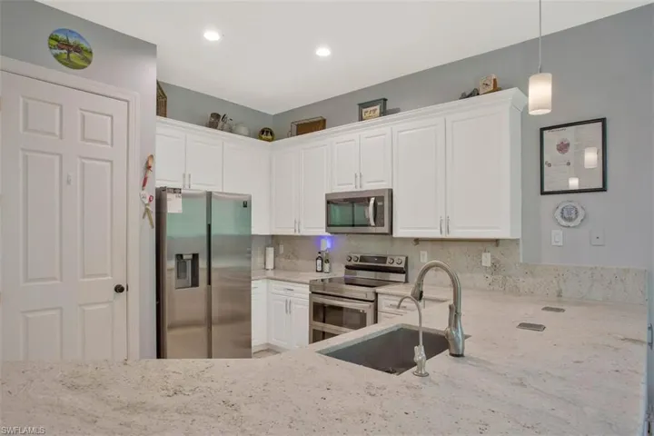 Kitchen featuring white cabinets, stainless steel appliances, light stone counters, and pendant lighting