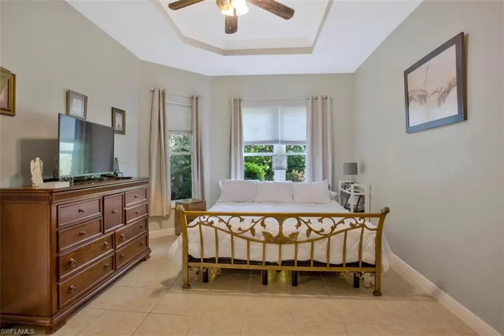 Bedroom with ceiling fan, a tray ceiling, and light tile patterned floors