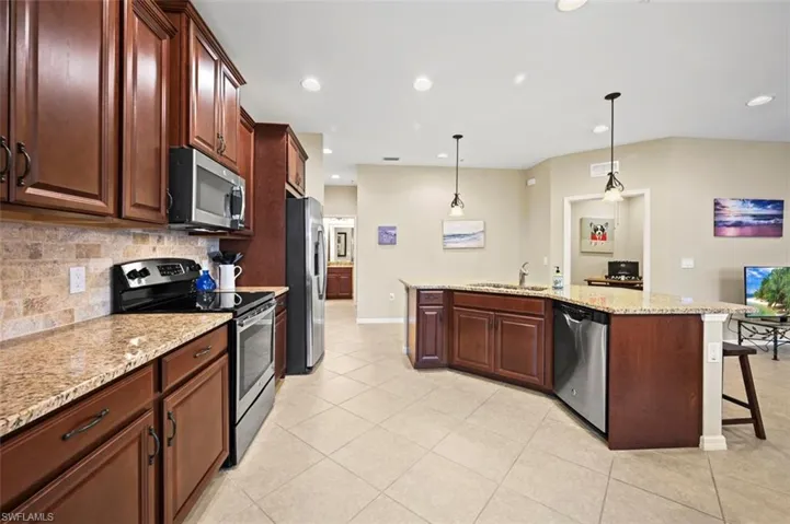 Open floor plan with spacious kitchen featuring stainless steel appliances, tile backsplash, large kitchen island with counter seating, and dining area.