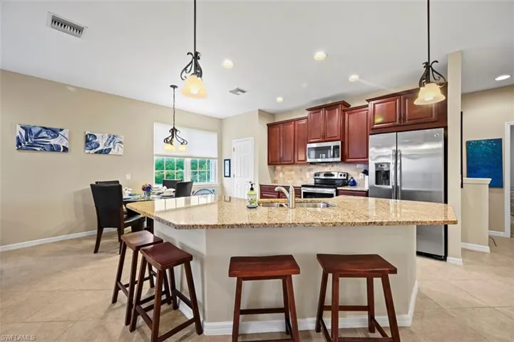 Open floor plan with spacious kitchen featuring stainless steel appliances, tile backsplash, large kitchen island with counter seating, and dining area.