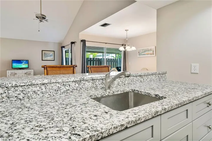 Kitchen with light stone counters, a ceiling fan, pendant lighting, a chandelier, and vaulted ceiling