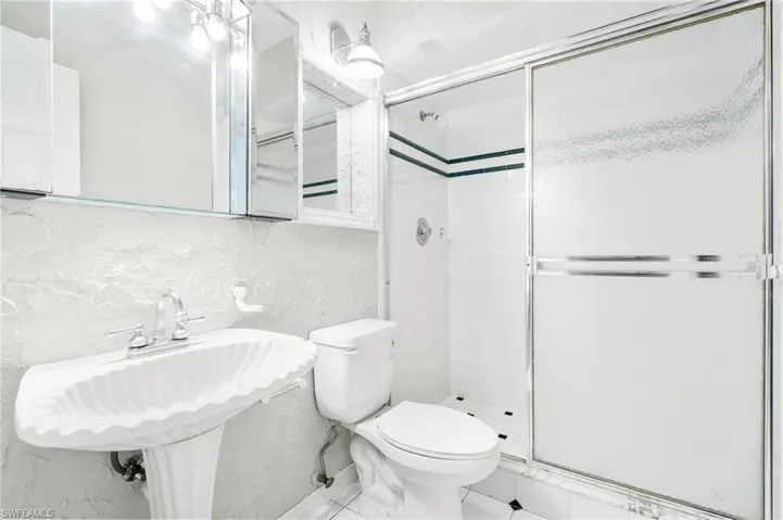 Bathroom featuring a shower stall, a textured wall, and tile patterned floors