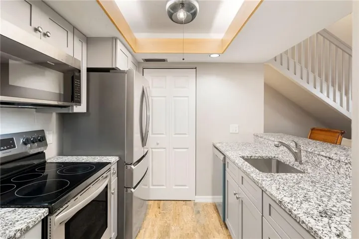 Kitchen with stainless steel appliances, gray cabinets, light stone counters, and light wood-type flooring