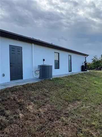 Rear view of house featuring central AC unit, a lawn, and stucco siding