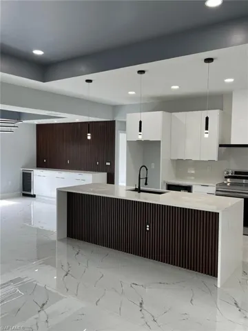 Kitchen featuring modern cabinets, decorative light fixtures, stainless steel electric stove, light countertops, and a sink