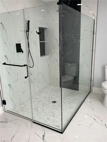Full bath with toilet, marble finish floor, and a marble finish shower