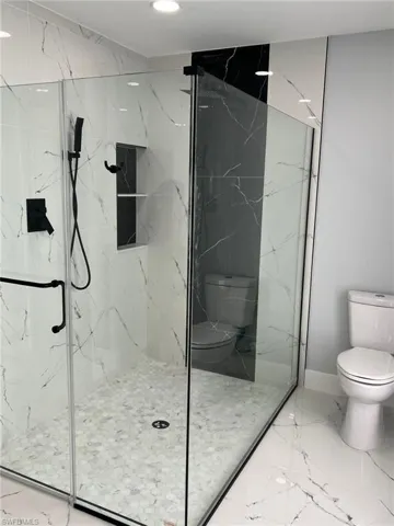Bathroom featuring a marble finish shower, marble finish floor, and toilet