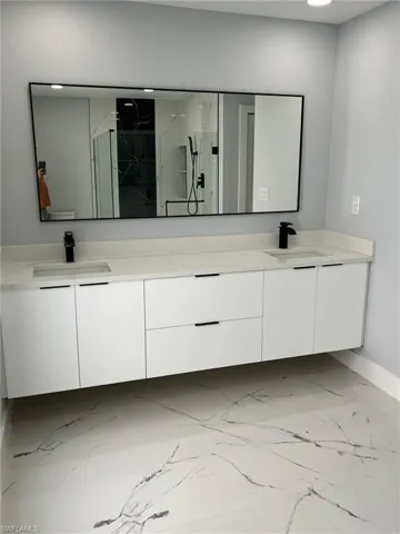Bathroom with marble finish floor, double vanity, a sink, and a marble finish shower