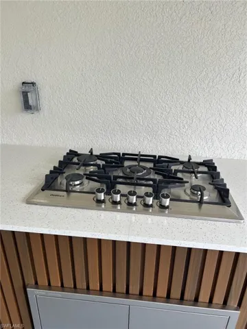 Details with a textured wall, brown cabinetry, gas cooktop, and light stone countertops