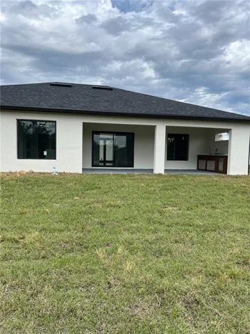 Back of house featuring a patio area, roof with shingles, a lawn, and stucco siding