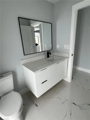Bathroom featuring toilet, marble finish floor, baseboards, and vanity