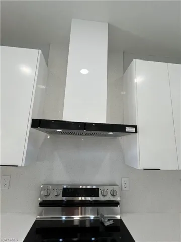 Kitchen with white cabinets, light countertops, wall chimney range hood, electric stove, and modern cabinets