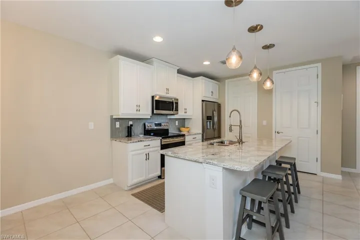 Kitchen features upgraded white cabinetry and large center island with sink and modern decorative light fixtures