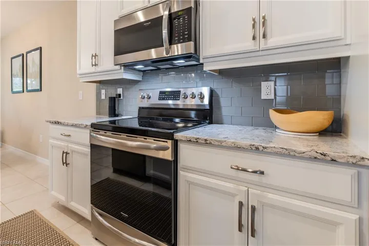 Kitchen featuring white cabinets, appliances with stainless steel finishes, glass tile backsplash