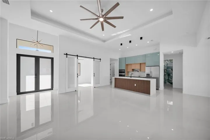 Unfurnished living room featuring a tray ceiling, a barn door, a high ceiling, a ceiling fan, and recessed lighting
