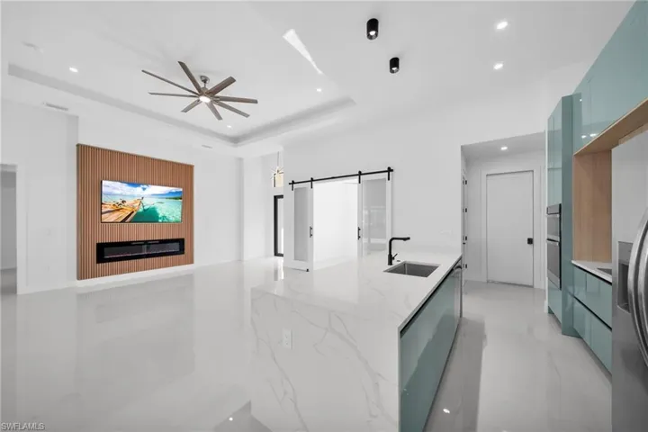 Kitchen with a barn door, light stone counters, ceiling fan, stainless steel refrigerator with ice dispenser, and light marble finish floors