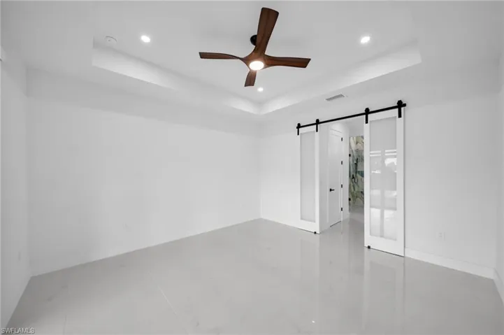 Unfurnished bedroom with a raised ceiling, a ceiling fan, a barn door, recessed lighting, and ensuite bath