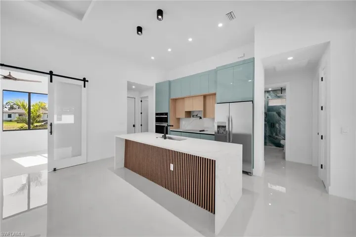 Kitchen with stainless steel fridge, a center island with sink, modern cabinets, a barn door, and light stone counters