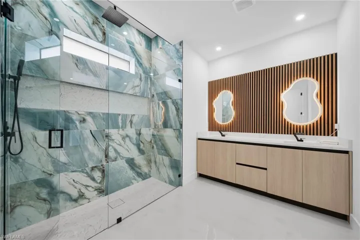 Full bath featuring a marble finish shower, double vanity, and recessed lighting