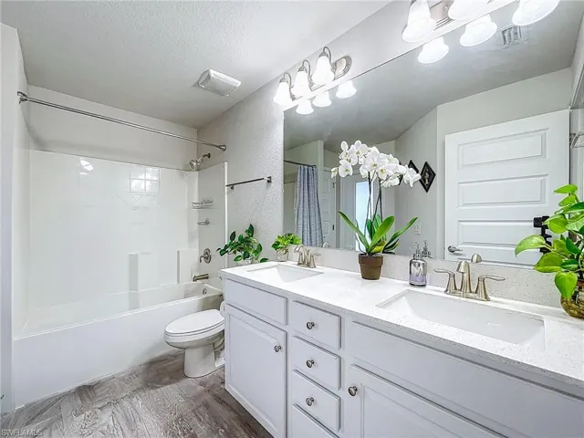Bathroom featuring double vanity, shower / bath combo with shower curtain, wood finished floors, and a textured ceiling