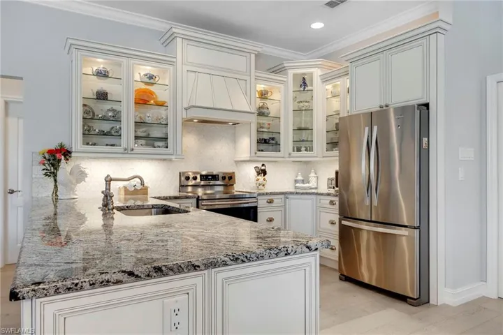 Kitchen with light hardwood / wood-style floors, custom range hood, appliances with stainless steel finishes, backsplash, and sink
