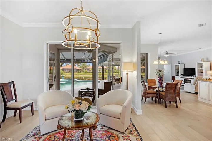 Living room with ornamental molding, light wood-type flooring, and ceiling fan with notable chandelier